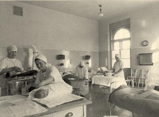 iz zgodovine medicine Soba v porodnišnici na Šlajmerjevi ulici v Ljubljani v šestdesetih letih 20. stoletja z babicami, ki otročnicam prinašajo novorojenčke v dojenje (foto Vlastja Simončič).