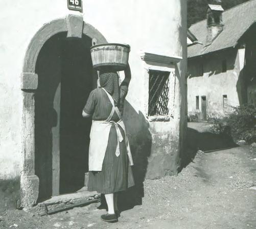 Žena nese škaf z vodo. Kamna Gorica leta 1955. A woman carries a wooden pail of water. Kamna Gorica, 1955. imelo težave z oskrbo z vodo.