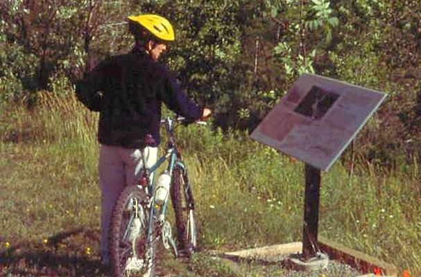 Bicyclist reading interpretive sign on Genesee Valley Greenway, a rail-trail along former Genesee Valley Canal.