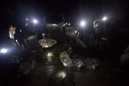 In this May 13, 2015 photo, residents wear headlamps as In this May 14, 2015 photo, workers carry a pallet of they hunt for translucent "glass eels," using mosquito briquettes, a biofuel substitute