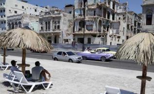 People sit on deck chairs on an artificial beach as a bride and groom ride by in a convertible on the Malecon in Havana, Cuba, Thursday.