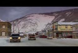 Dawson City: Wide static shot of Dawson City town with trucks and cars driving down street (Winter) 02:50:53:14 N 02:51:00:15