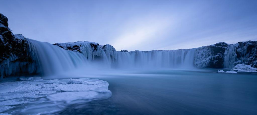 Brilliant blue glacial water cascades over Godafoss on a snowy day in Northern Iceland. Want to visit the north?