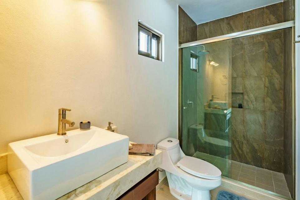 The bathroom, as all bathrooms has a vanity, with marble top, covered shower with aluminum railing and tempered glass, light
