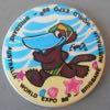 Lot # 319 - Plastic Refrigerator Magnet picturing a multicolor duckbilled platypus wearing a swim suit and cap while running on the beach with sea stars and sea shells at his feet.
