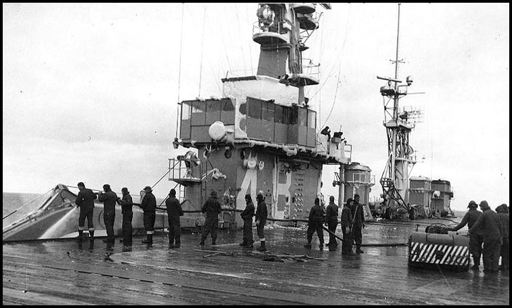 Crewmen wash snow and ice from the flight deck and superstructure, during Operation Icecap. Ice is visible on the island and mast.