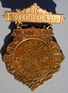 Lot # 109 - "Michigan" Brass hanging badge, Eglit # 471. Badge with die-cut edge has a decorative scroll design. "Michigan" on the bar at top.