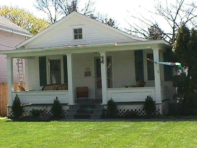 Flat roofed, full-width front porch with slender square columns and solid wood rail.