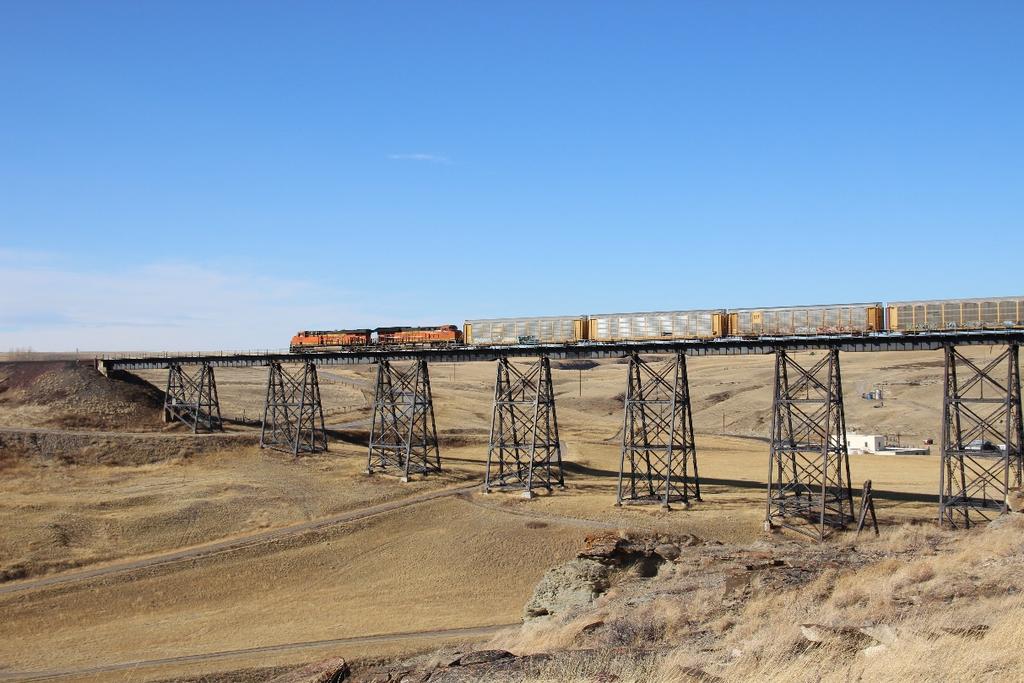 BNSF 6983, a GE ES44C4, and BNSF 3933, a GE ET44C4, with a train of autoracks, cross the large trestle at the west side of Cut Bank,