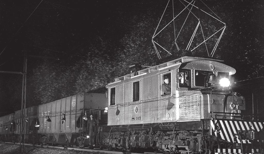 The photographer s flood lamps illuminate T S-05 electric locomotive pulling a load of coal cars at the uena interchange yard adjacent to raceland emetery, in this 965 view.