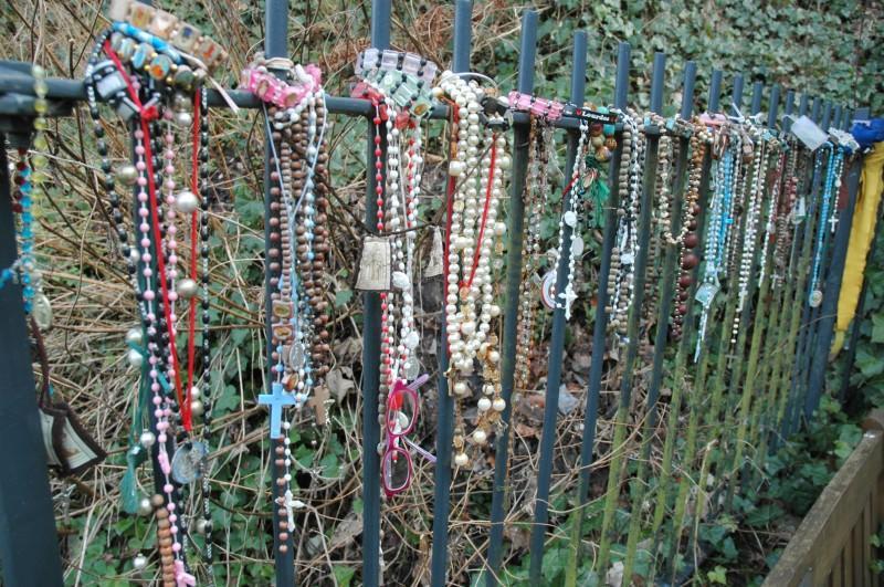 A well-worn statue of St Winefride in the gardens Rosary beads hung on railings by the shrine Although the shrine had only two other visitors while I was there (early March), the railings by the