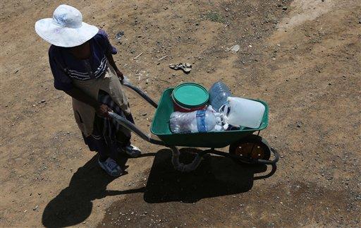 In this Thursday Jan. 7, 2016 photo, an elderly woman waits with containers in a wheelbarrow to collect free water in Senekal, South Africa where taps and water sources have run dry.