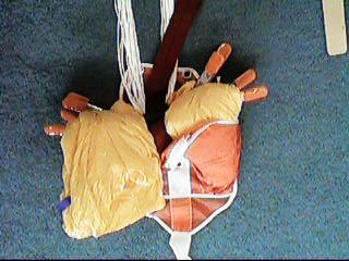 Raise parachute 4 inches and slide d-bag under parachute until bottom edge of closing flap lays under lower edge of canopy.