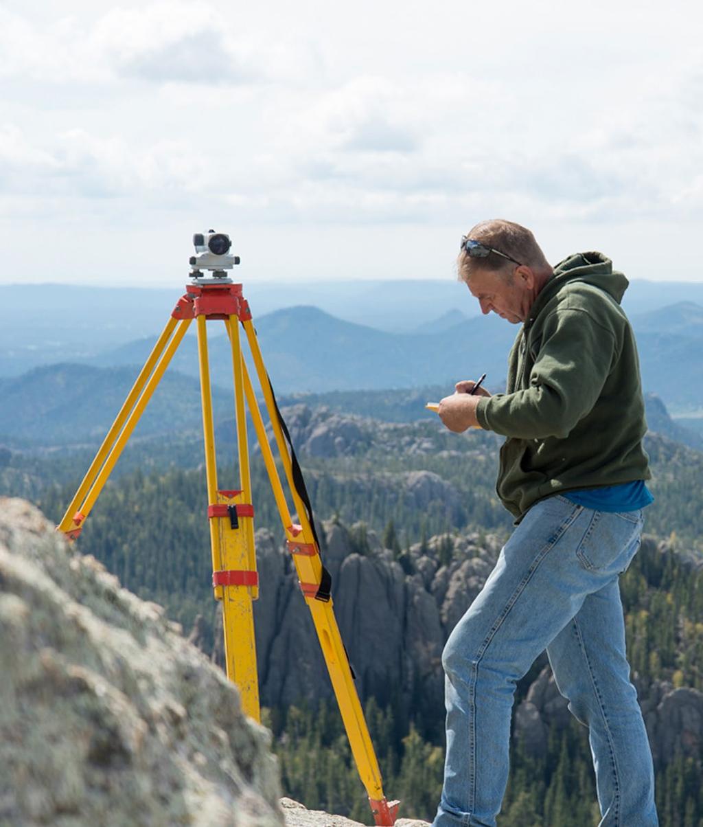 With a Sokkia B-1 level precariously set up near the lookout tower, Jerry Penry records the reading to the nearby points.