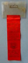 Lot # 339 - Fireman's Badge. Plastic holder with a suspended red ribbon with gold writing on it.