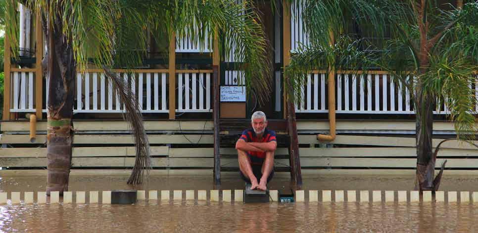 A local resident sits outside his home surrounded by flood waters on 6 January, 2011 in Rockhampton (Source: Getty Images).