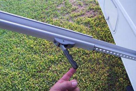 To close the awning: loosen the black knob, depress the grey tab at the upper end of each arm to release the inner arm.