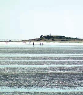 View of Hilbre Island from West Kirby with walkers at low tide.