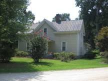 The house has gable returns and a hipped-roof porch on slender columns. The house retains its standing seam metal roofs.