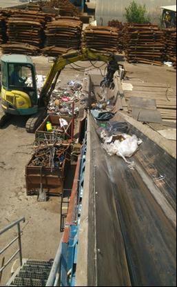 Vsebina kesona z odpadno mešano embalažo se je iztresla v oziroma pred zbirnik odpadkov, iz katerega poteka trak na sortirno linijo.