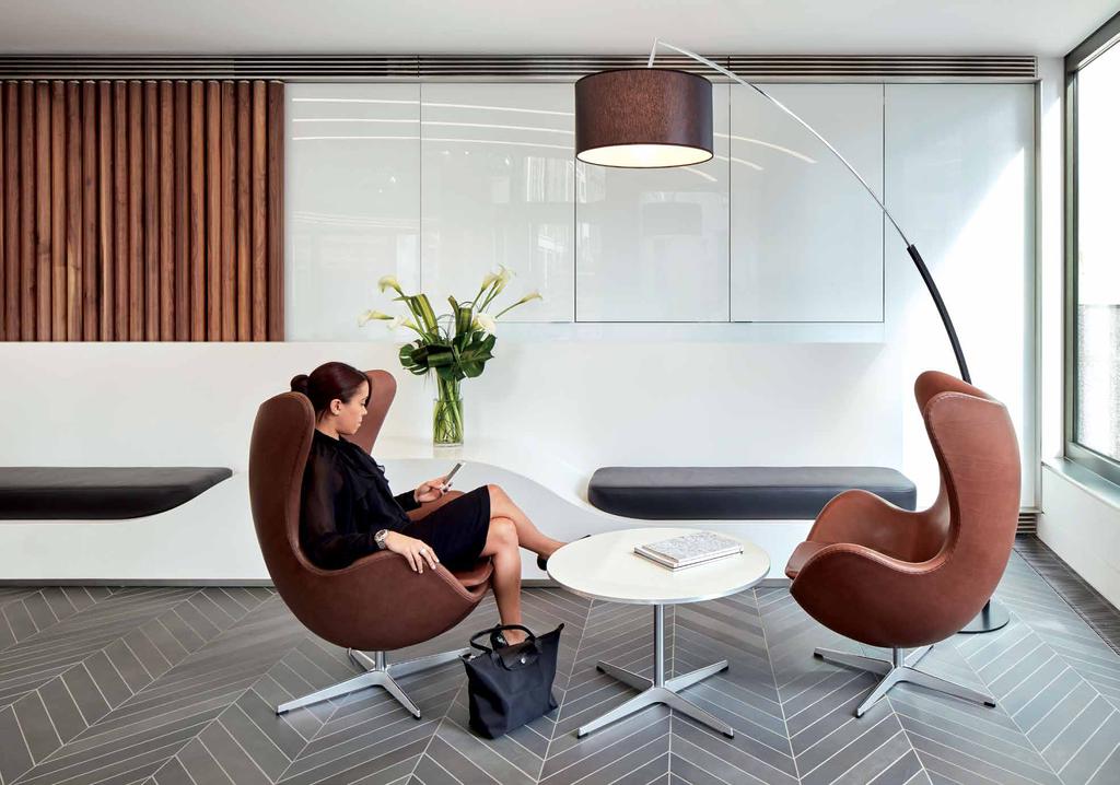 R E L A X & T A K E A S E A T The reception features a smooth white corian reception desk and seating pods, with American walnut feature walls and grey ceramic herringbone