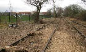 the school play area to the left and properties on Tarragon Place beyond. In the summer, low lying vegetation including grasses and ruderals currently covers the railway line.