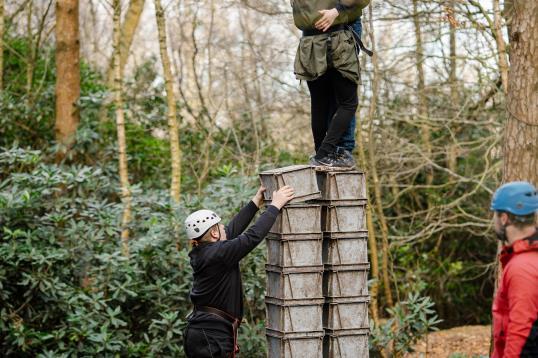 Crate Stack Challenge: In three small groups, young people take it in turn to either ascend a tower of crates, help the instructor stack the crates, or keep the ropes tight for those climbing.